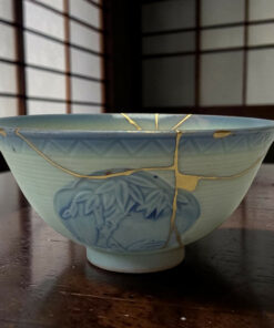 Two light blue ceramic bowls stacked and wrapped with beige string, resting on a dark wooden surface with a blurred wooden lattice background.