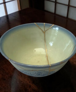 Ceramic bowl with gold kintsugi repair on a dark wooden table.