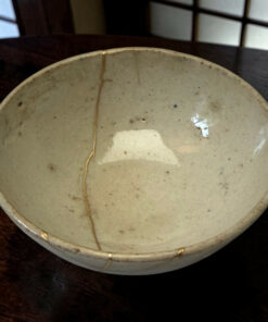 Close-up of a light gray speckled ceramic plate with a visible hairline crack running from edge to center on a dark wooden table.