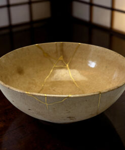 Beige ceramic bowl with thin gold string decorations on a dark wooden table.