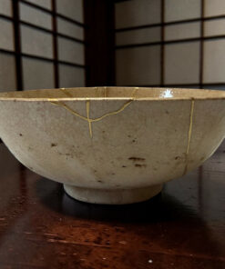 Close-up of a white ceramic bowl with visible cracks and stitched seams, resting on a dark wooden table.
