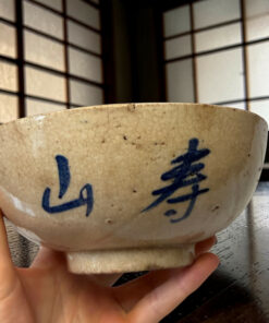 Close-up of a beige ceramic bowl with blue decorative strokes, held by a child’s hand.