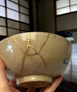 Child’s hands cradle a large round ceramic pot with yellow string arranged on its surface, set on a wooden table.