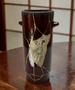 Dark ceramic vase with gold crackle pattern on a polished wooden table, background shelves blurred in a room setting