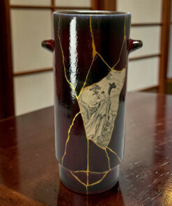 Close-up of a dark ceramic vase with gold crackle patterns on a wooden table, blurred background behind it.
