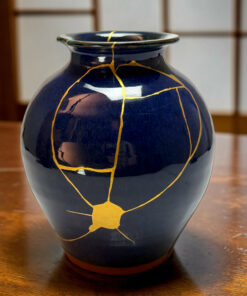 Close-up of a dark blue ceramic vase with gold crackle lines on a wooden table.