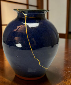 Close-up of a dark blue ceramic vase with a gold crack repair running down its surface (kintsugi).