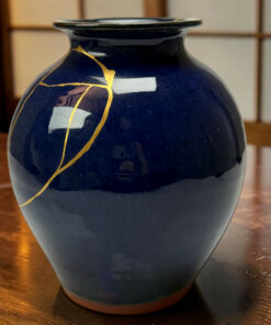 Blue ceramic vase with gold kintsugi cracks, shown in close-up on a wooden table.