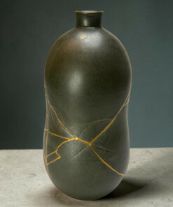 Close-up of a dark ceramic vase with gold crackle lines, set on a concrete floor against a gray background.