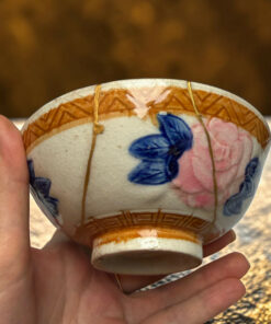 Close-up of a hand holding a decorated ceramic egg with blue and pink floral patterns and gold lines.