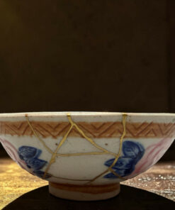 Decorative ceramic hanging planter with a beige rope lattice, blue floral patterns, resting over a wooden surface against a dark background.