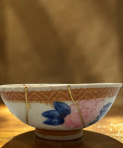 Decorative ceramic bowl with blue and pink floral pattern, hung by cords above a wooden table in warm light.