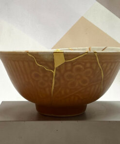Close-up of a brown ceramic planter with yellow straps, on a light pedestal against a pale geometric background.