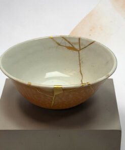 White ceramic bowl with a gold crackle glaze pattern, placed on a display pedestal in a neutral setting