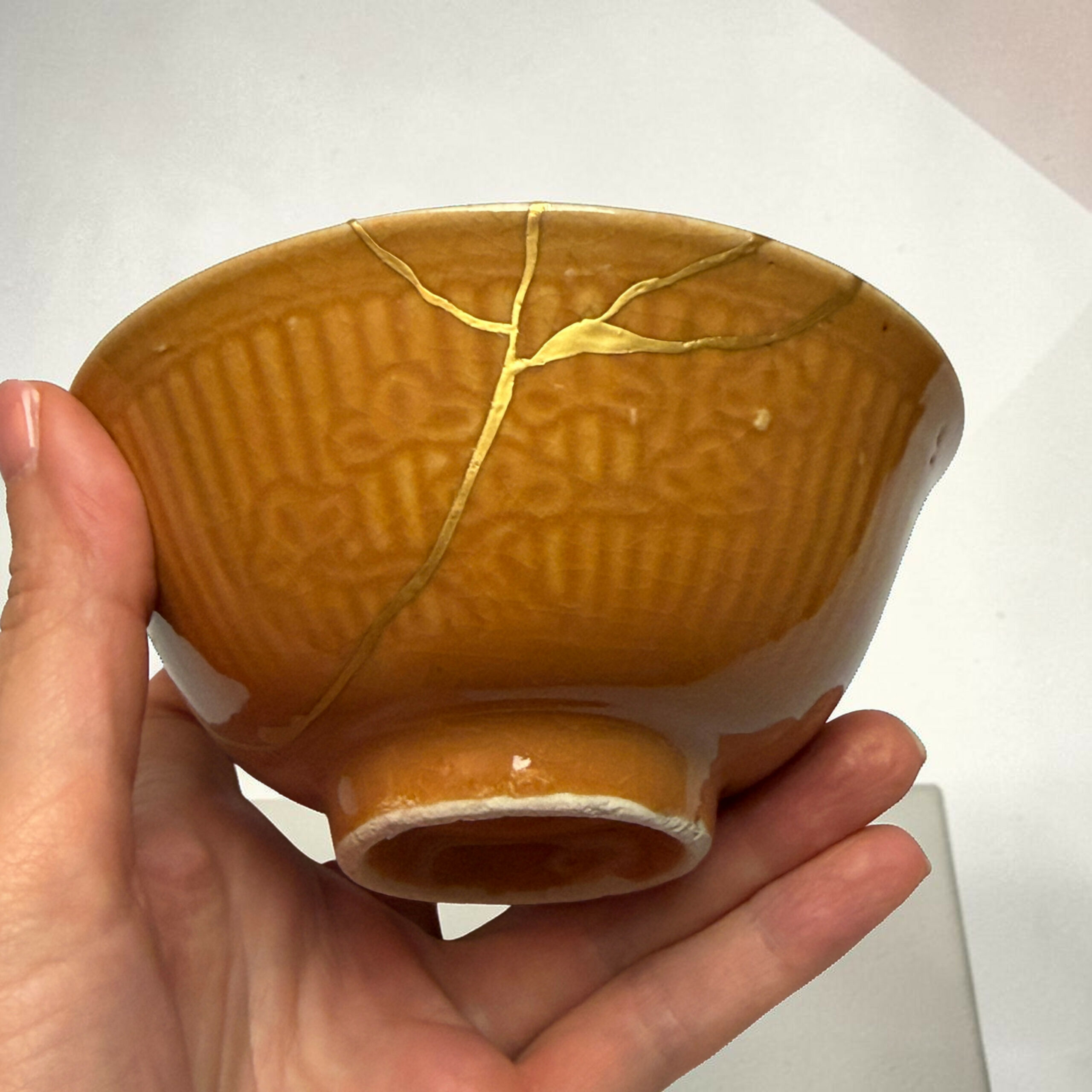 IMG_2506-Photoroom | Kintsugi by Myriam GREFF Close-up of a small round brown bread roll with pale dough strips across the top, held in a hand.