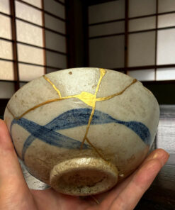 Close-up of a hand holding a smooth stone with gold-veined cracks, set against a dark, slatted background.