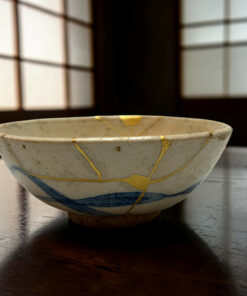 Close-up of a white ceramic bowl with blue rim and gold decorative lines on a dark wooden table.