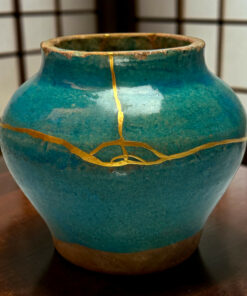Close-up of a teal ceramic vase showing a gold crackle seam and weathered rim against a grid-pattern background.