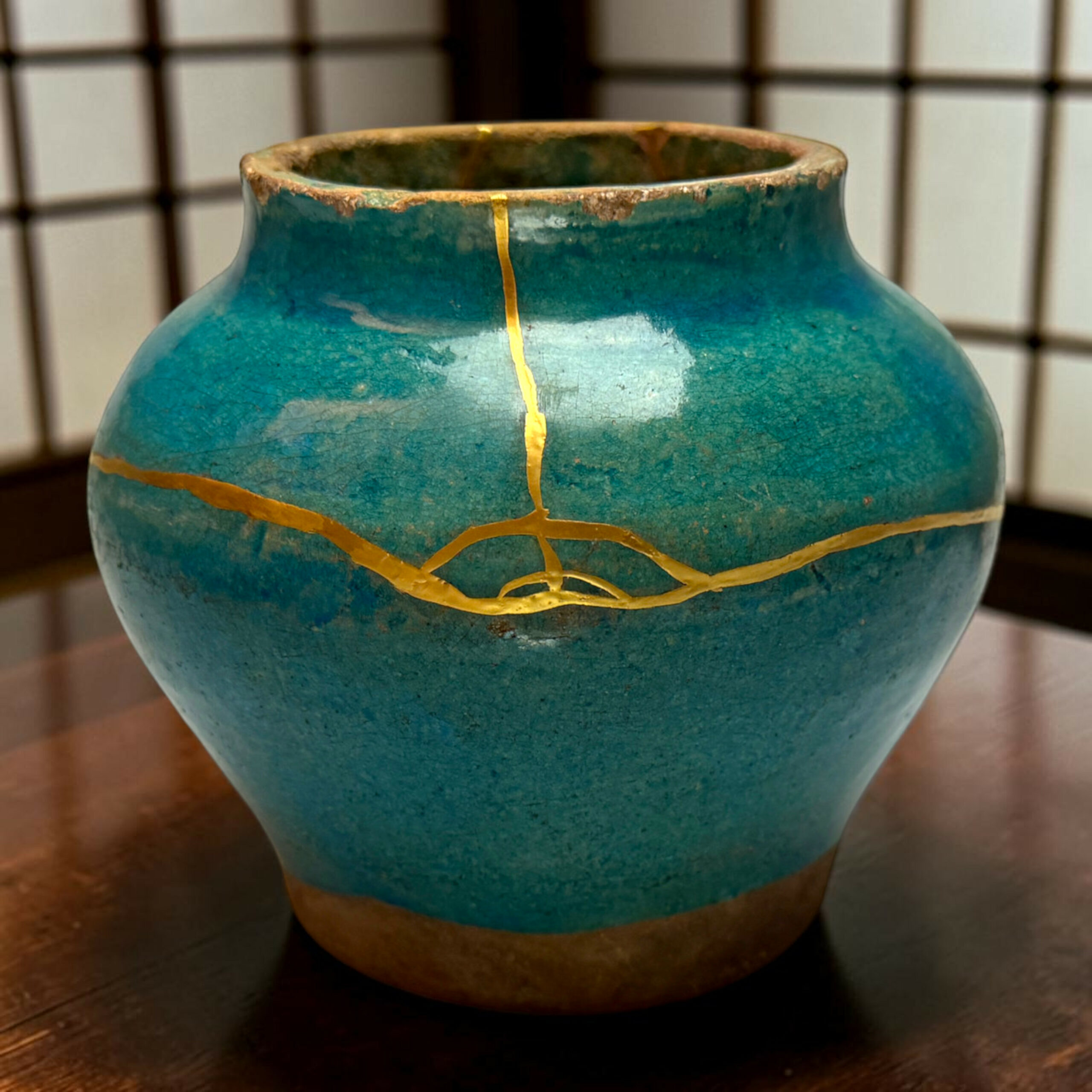 IMG_2514-Photoroom | Kintsugi by Myriam GREFF Close-up of a teal ceramic vase showing a gold crackle seam and weathered rim against a grid-pattern background.