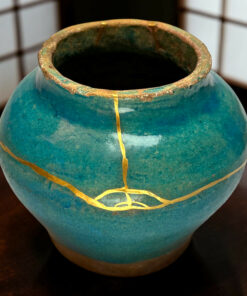 Close-up of a turquoise ceramic vase with a wide opening and gold decorative lines around its rim and body.