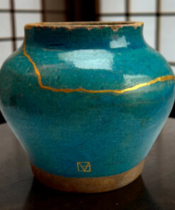 Close-up of a turquoise ceramic vase with a chipped rim and gold crackle lines.