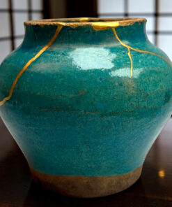 Close-up of a turquoise ceramic vase with gold cracks in a crackled glaze, resting on a dark wooden surface.