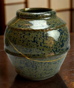 Close-up of a blue-green ceramic vase neck with a mottled glaze and a yellow cord, on a wooden table.