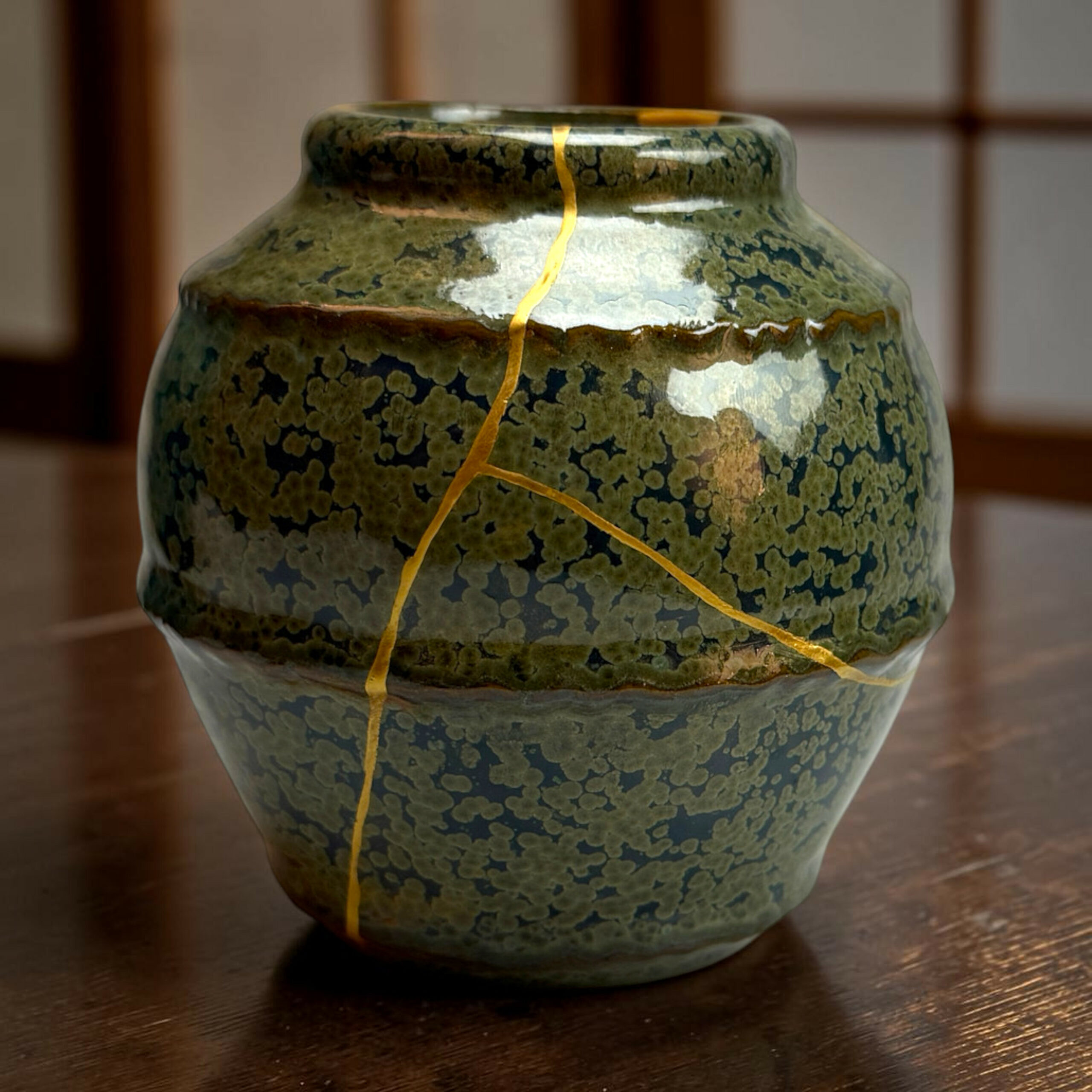 IMG_2521-Photoroom | Kintsugi by Myriam GREFF Close-up of a green-glazed ceramic vase with a crackled surface and a yellow string wrapped around its neck.
