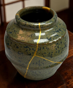 Close-up of a green glazed ceramic vase with gold decorative lines on a wooden floor.
