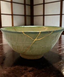 Green glazed ceramic bowl wrapped with string rests on a polished wooden table, with a lattice screen in the background.