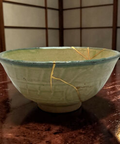 A green ceramic bowl with a gold string wrapped around its rim, placed on a dark wooden surface against a grid-patterned background.