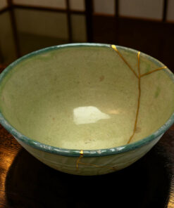 Close-up of a green glazed ceramic bowl with a yellow string wrapped around its rim, resting on a dark wooden table.