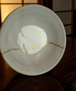 Close-up of a gray plate with a thin gold string wrapped around it, placed on a dark wooden floor.