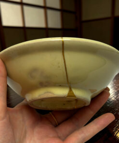 Close-up of a pale-green ceramic egg with a vertical brown seam being held in a hand.