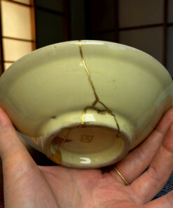 Close-up of a pale green ceramic egg with gold seams from kintsugi, held in cupped hands.