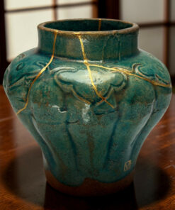 Close-up of a teal ceramic vase with gold kintsugi cracks visible on the surface.