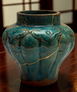 Close-up of a teal ceramic vase with gold decorative lines on a wooden table.
