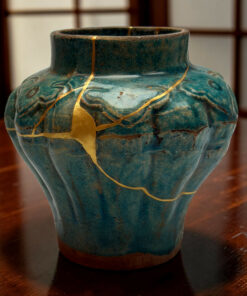 Close-up of a turquoise ceramic vase with gold crackle lines on a dark wood table