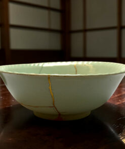 Close-up of a white ceramic bowl with a gold crackle glaze on a dark wooden table.