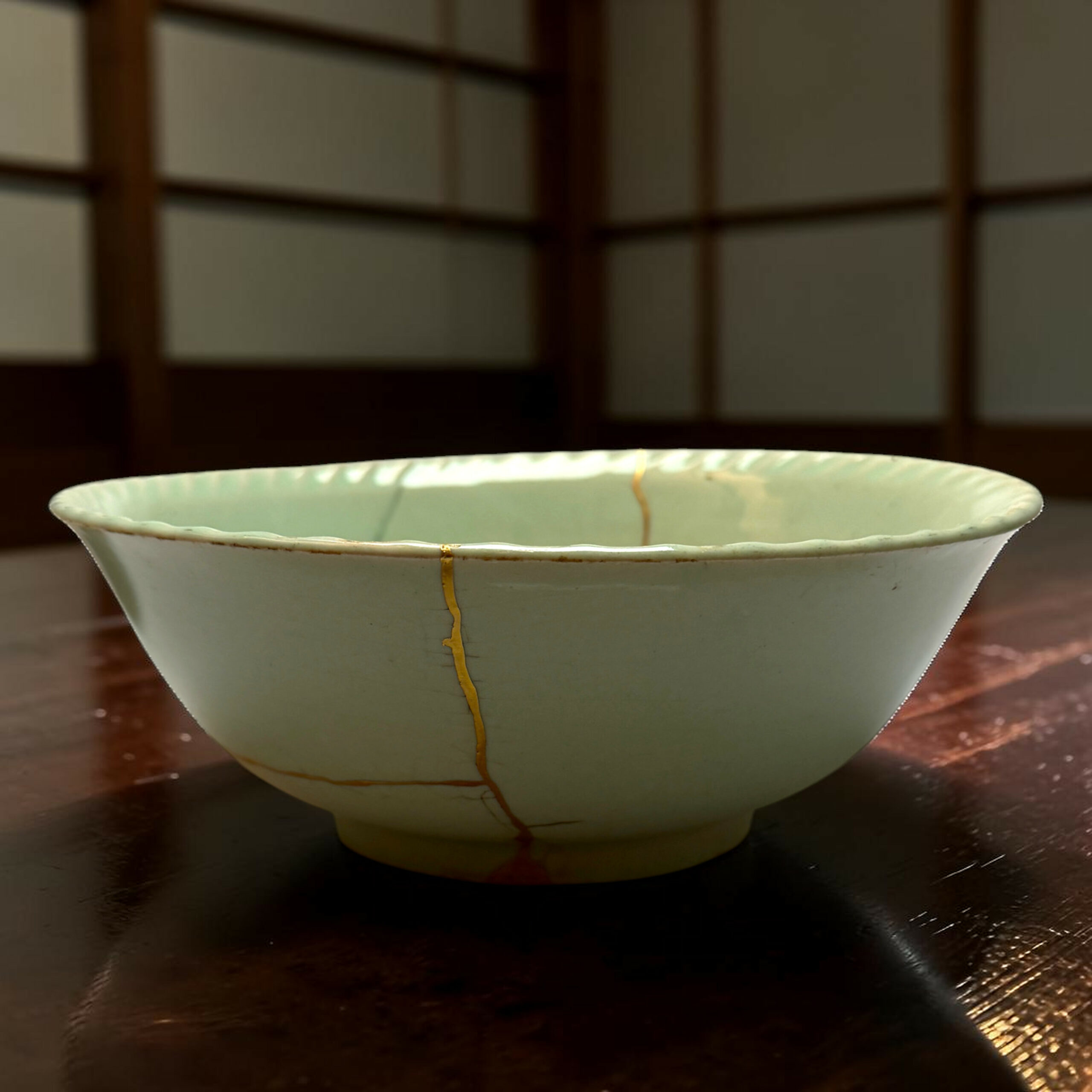 IMG_2539-Photoroom | Kintsugi by Myriam GREFF Close-up of a white ceramic bowl with a gold crackle glaze on a dark wooden table.
