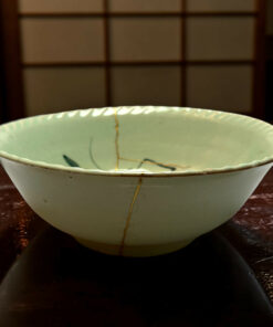 Close-up of a pale green ceramic bowl with a long brown crack running down its side on a dark wooden surface