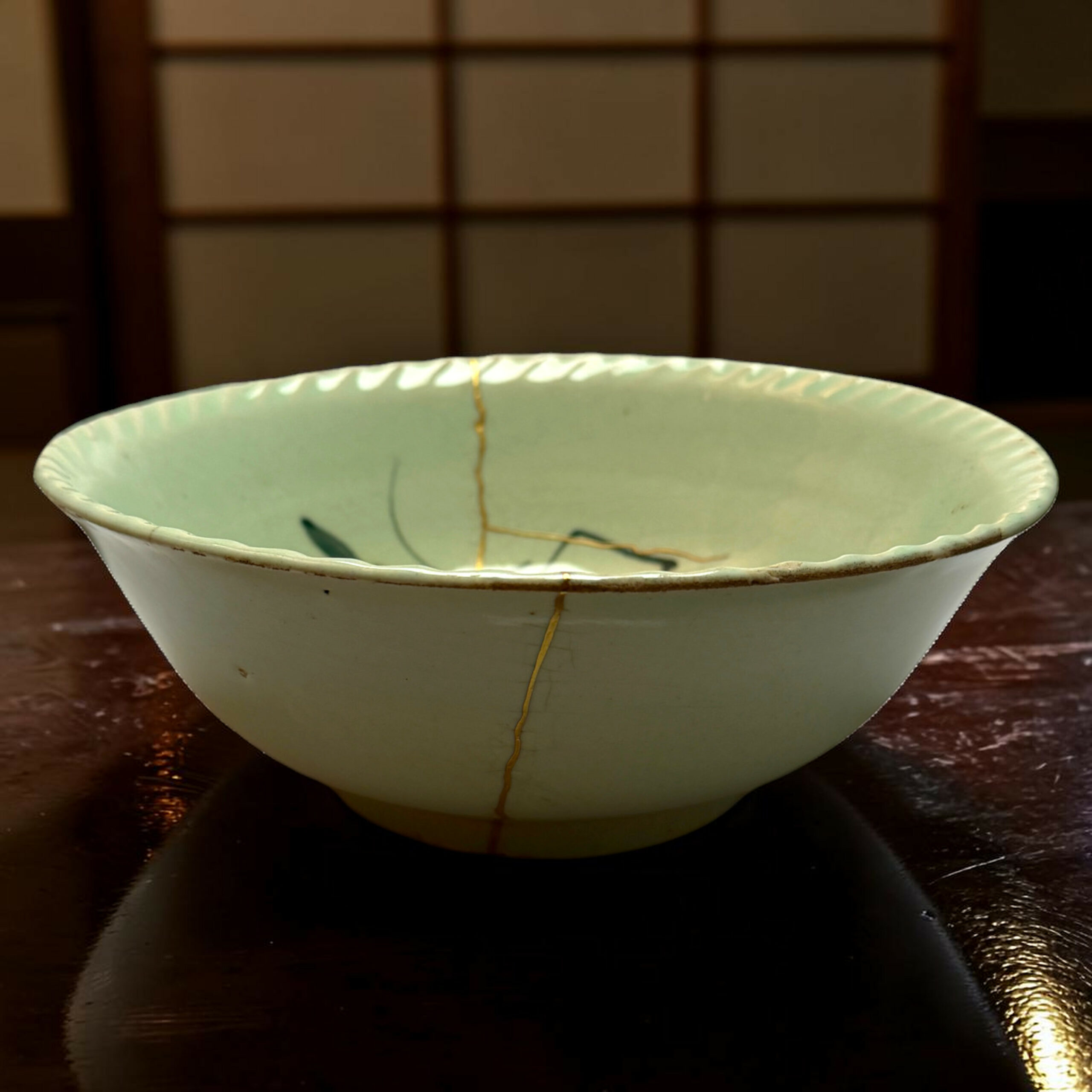 IMG_2540-Photoroom | Kintsugi by Myriam GREFF Close-up of a pale green ceramic bowl with a long brown crack running down its side on a dark wooden surface