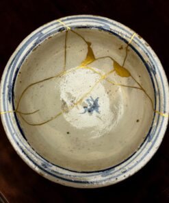 Close-up of a white ceramic plate with blue rim, showing gold kintsugi cracks.