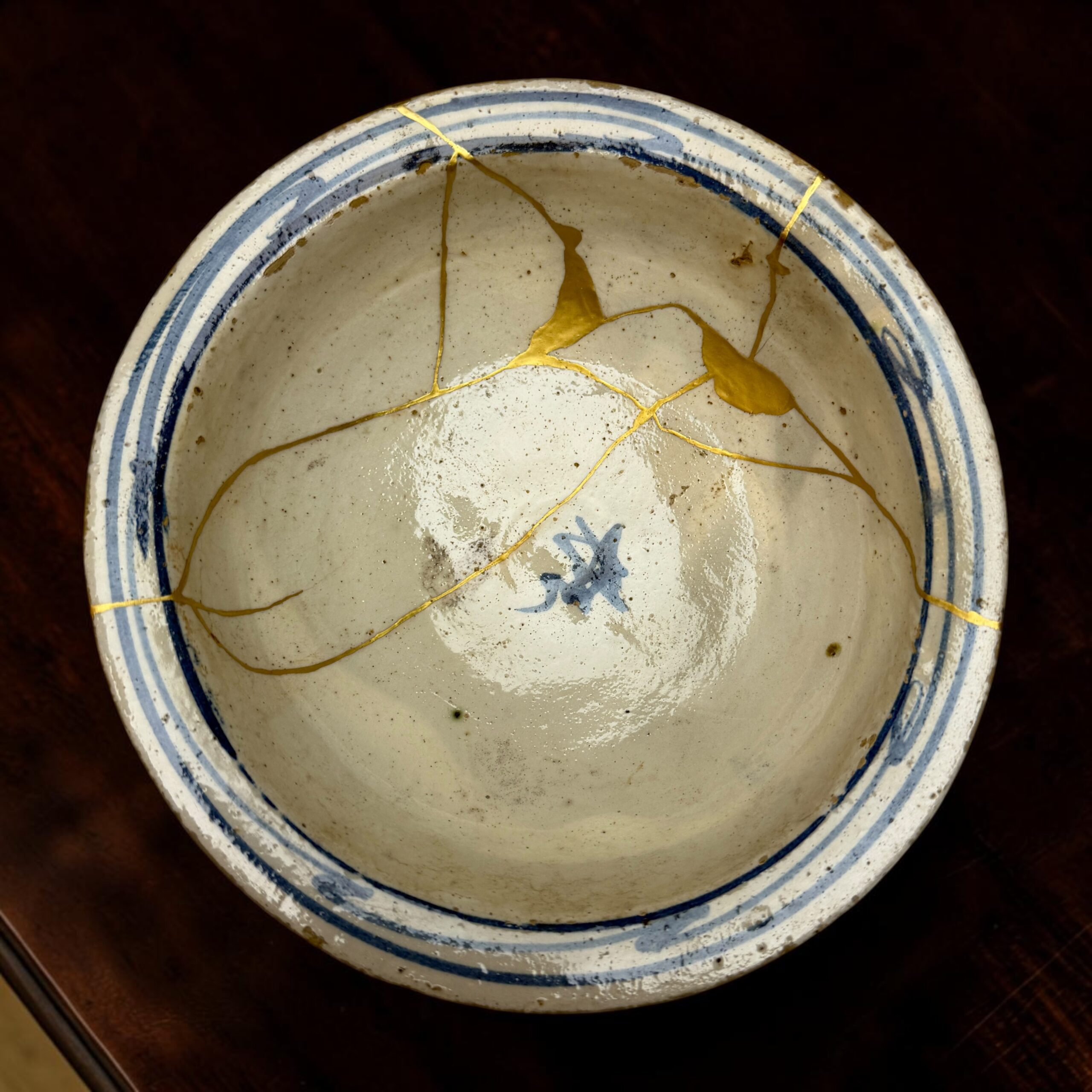 IMG_2549 | Kintsugi by Myriam GREFF Close-up of a white ceramic plate with blue rim, showing gold kintsugi cracks.