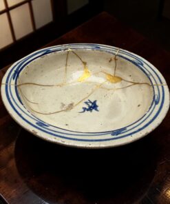 White ceramic plate with a blue rim and gold crackle lines, resting on a dark wooden table.