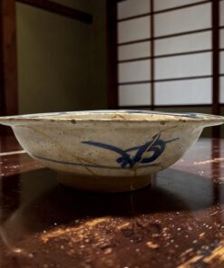 Close-up of a blue-and-white ceramic bowl on a polished wooden table with scattered crumbs around it.