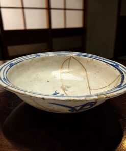 Close-up of a white ceramic bowl with blue rim on a wooden table, showing food remnants and thin brown sauce lines inside.