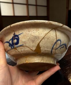 Close-up of a speckled ceramic bowl with blue designs being held by a person, indoors at a wooden table.