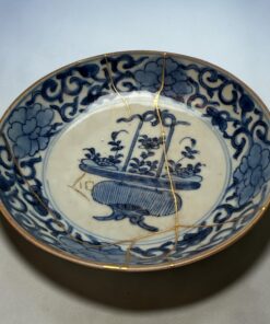 Close-up of a blue-and-white ceramic plate with a gold rim, bound by a thin gold string.