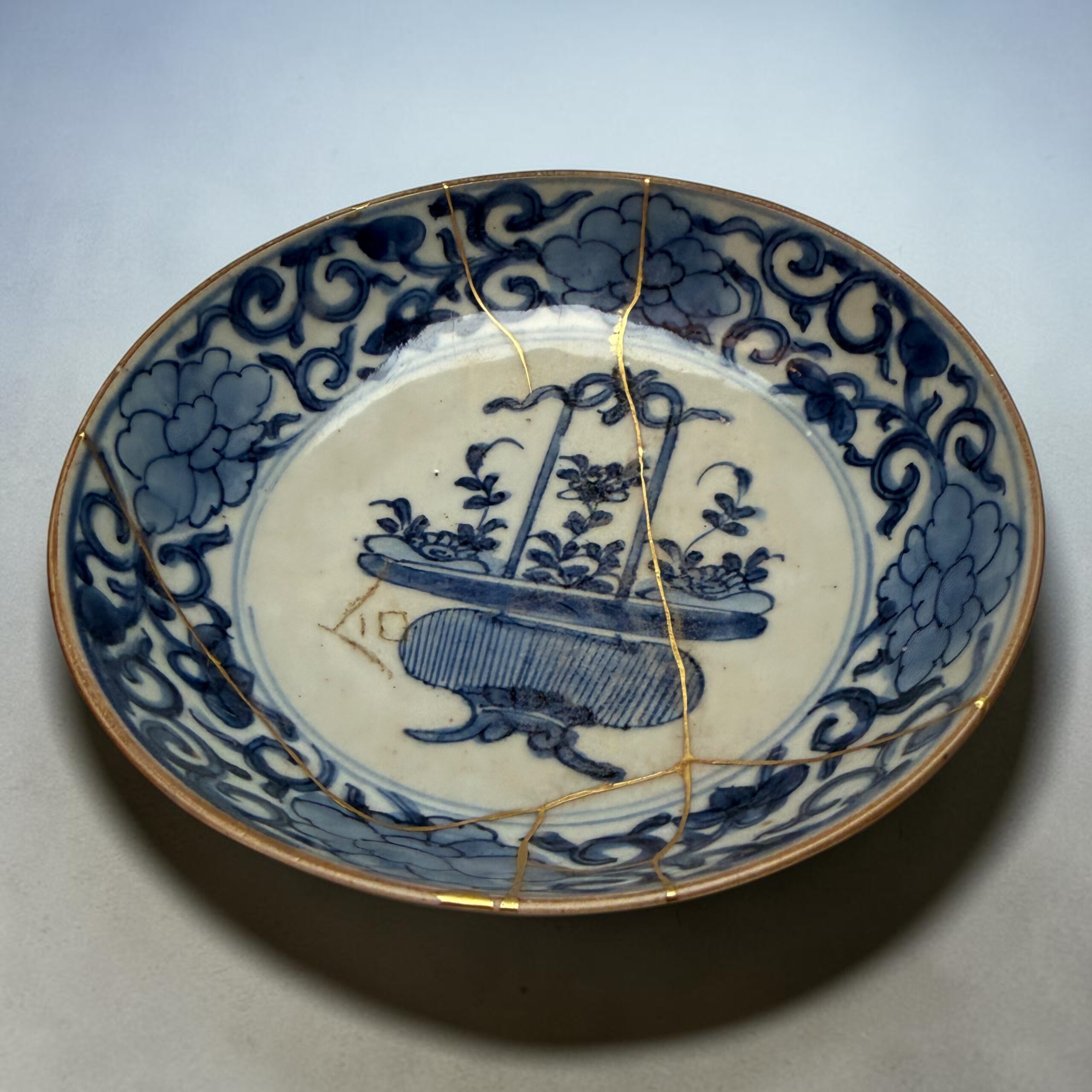 IMG_2556 | Kintsugi by Myriam GREFF Close-up of a blue-and-white ceramic plate with a gold rim, bound by a thin gold string.
